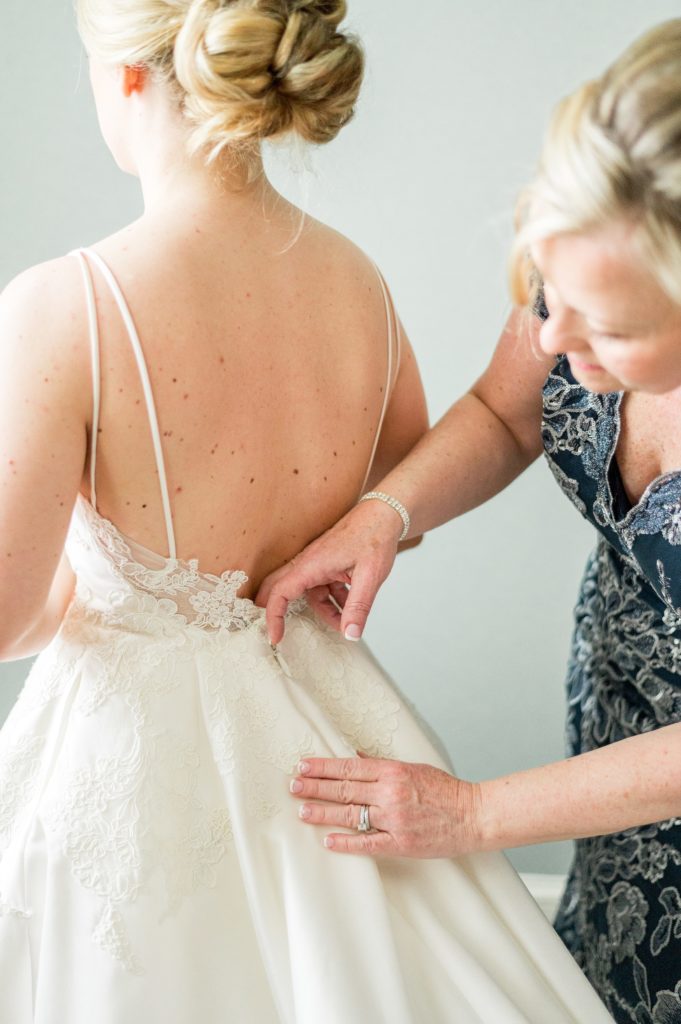 Bride putting on her wedding dress with the help of her mom. 