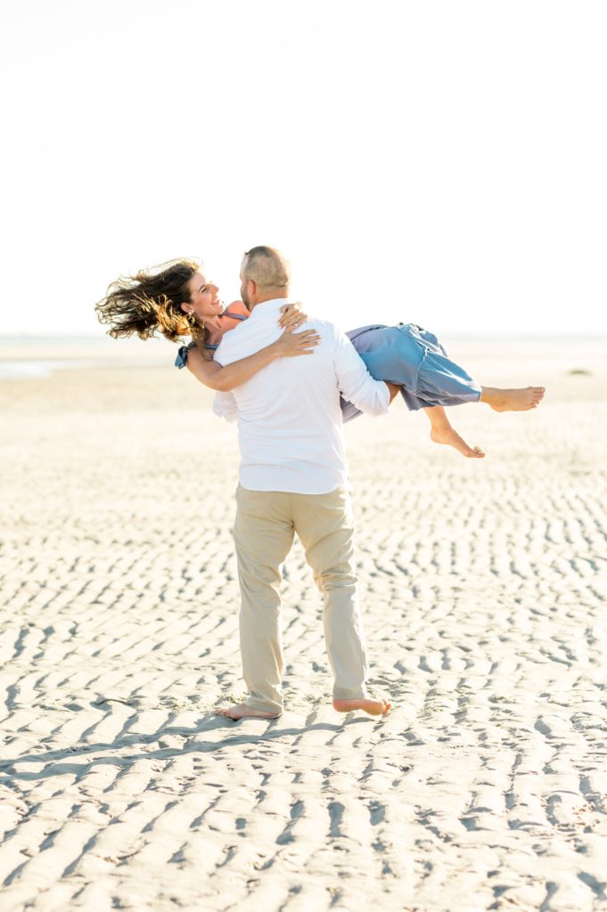 Man picking up his bride to be and spinning her around on the beach