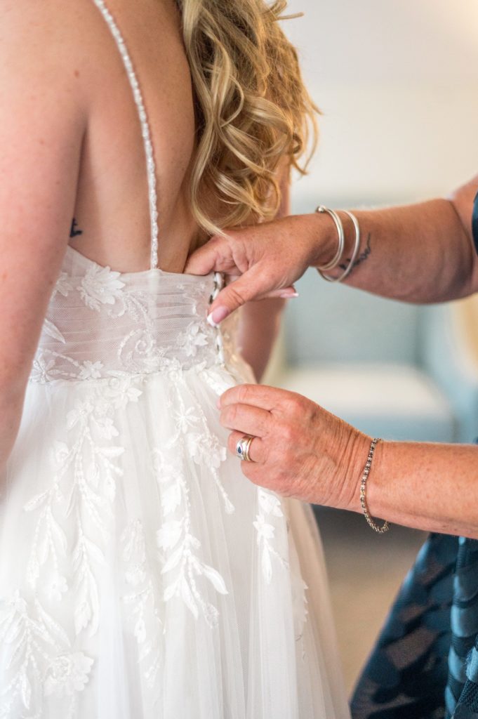 Mom buttoning the back of her daughters wedding dress 