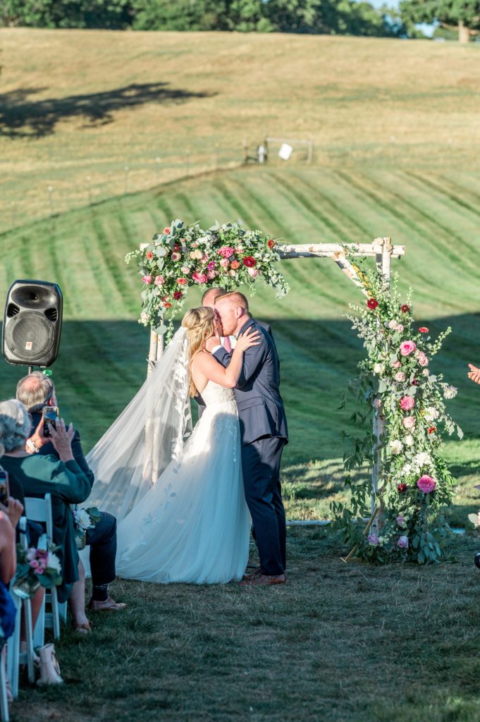 Bride and groom first kiss during outdoor ceremony at Gibbet Hill in Groton, MA