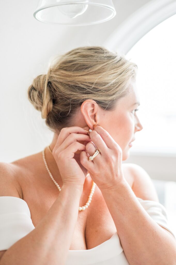 Bride getting ready by putting on jewelry for old hollywood styled wedding