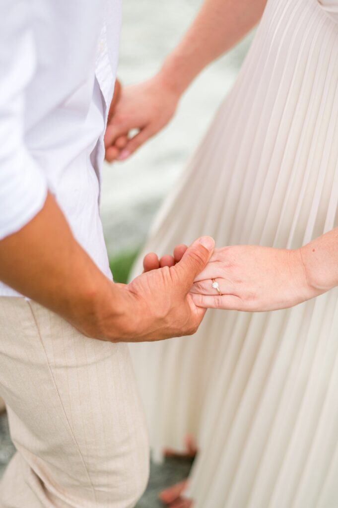 Close up detail photo of couple holding hands and engagement ring