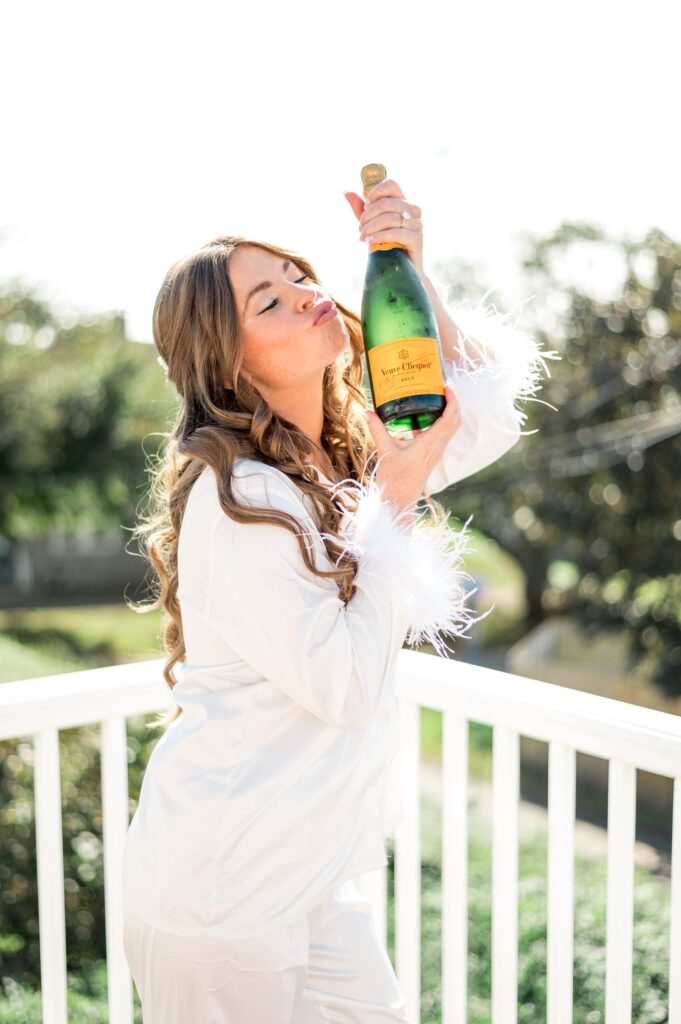 Bride holding champagne bottle during getting ready photos wearing silk PJs with feather sleeves
