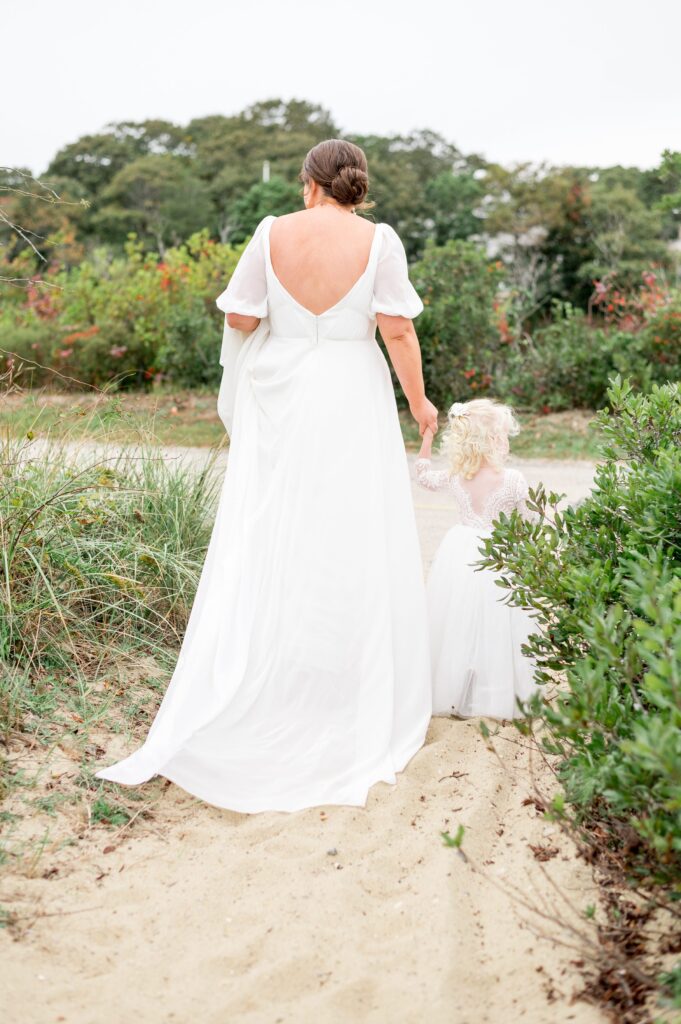 Bride and flower girl candid photo walking hand in hand on the beach 