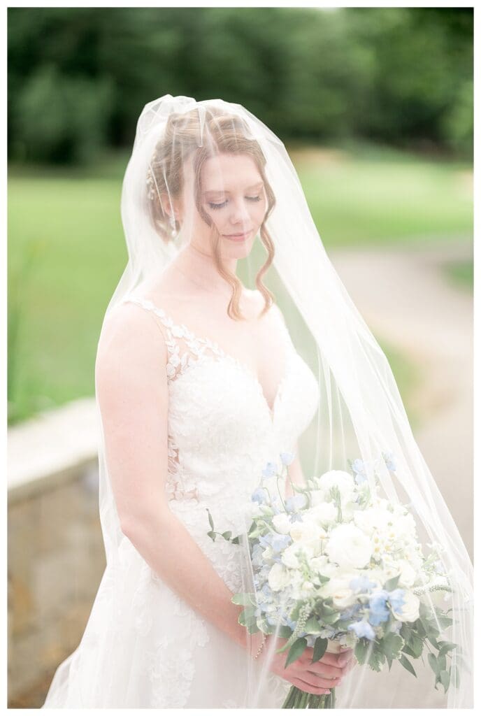Bride smiling softly under her veil holding a lush white and blue bouquet.