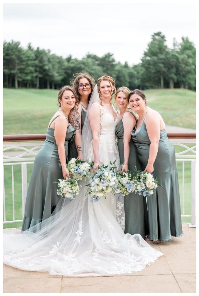 The bride and bridesmaids pose along the white railing with the golf course in the background.