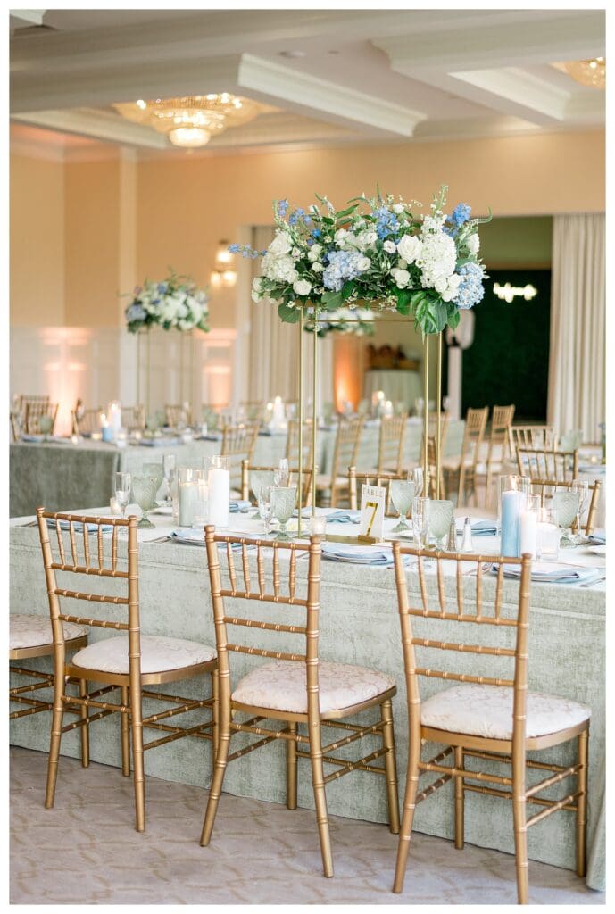 Reception room at Indian Pond Country Club with gold chiavari chairs and white and blue florals.