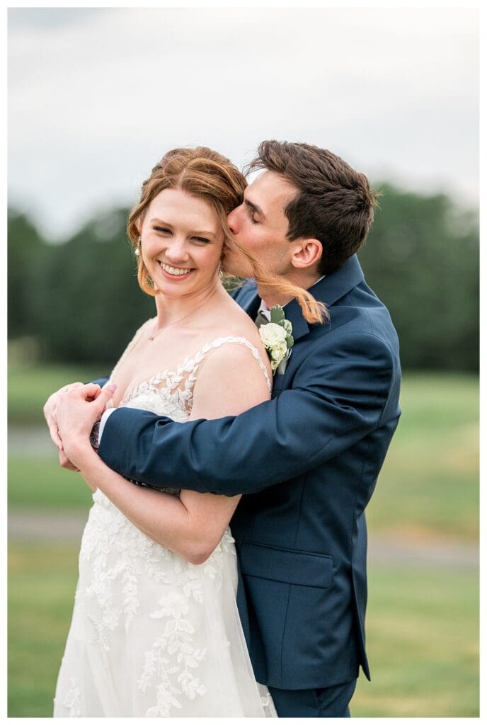 Bride and groom laughing and embracing on the green at Indian Pond Country Club.