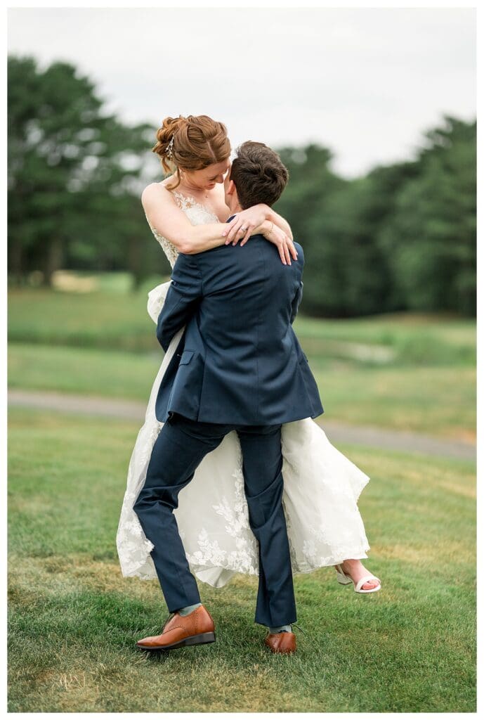 Groom lifts the bride off the ground in a joyful embrace on the lawn.