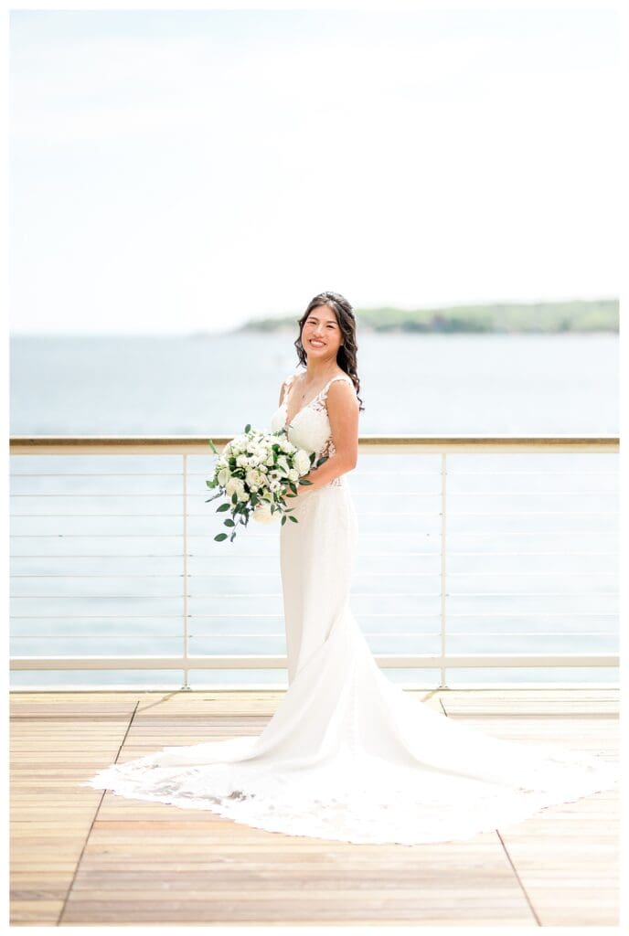 Bride holding bouquet of white roses and greenery in natural light.