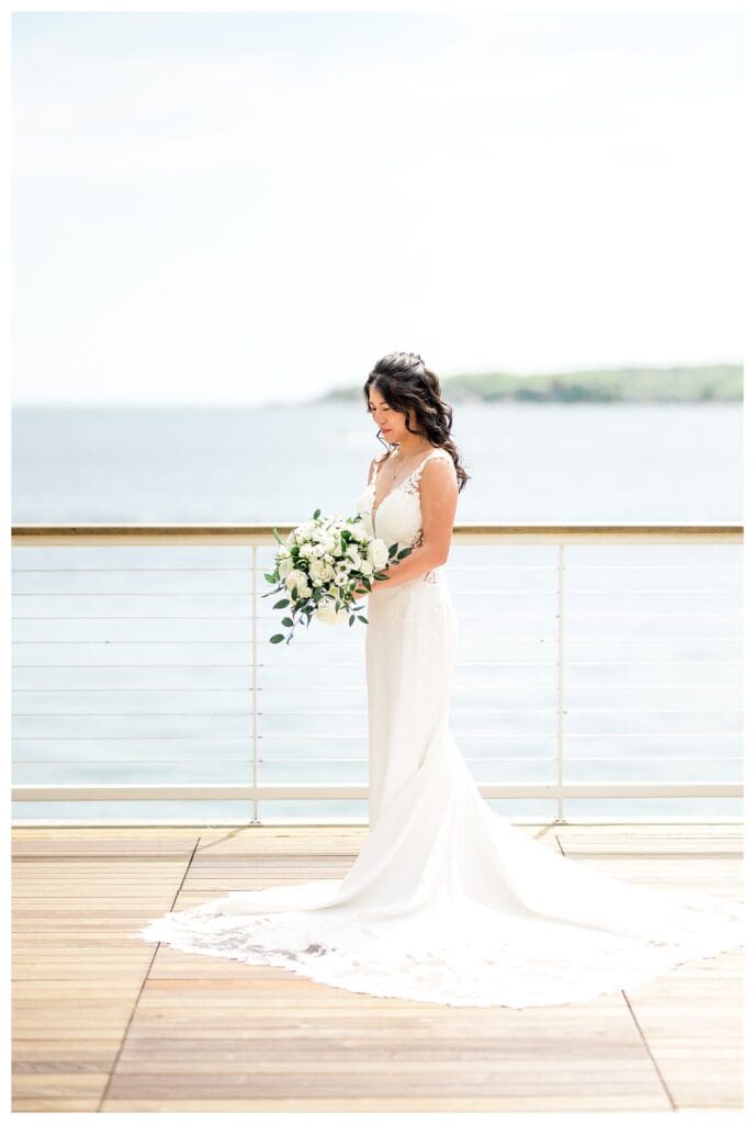 Bride standing on a white deck, holding her bouquet with the ocean behind her.
