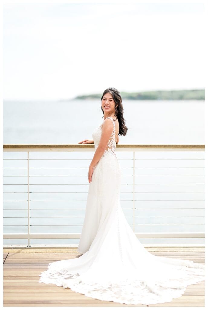 Bride leaning against white railings, ocean breeze in her hair during seaside portraits.