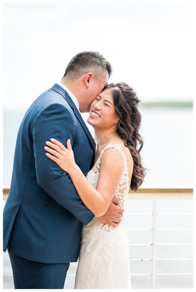 Bride and groom sharing a joyful embrace on the deck overlooking the ocean at a coastal Massachusetts wedding.