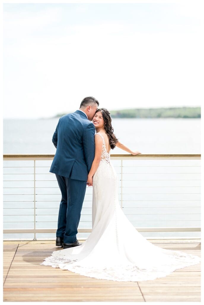 Beauport Wedding Photography: Bride and groom holding hands and smiling on a sunlit deck with ocean views.