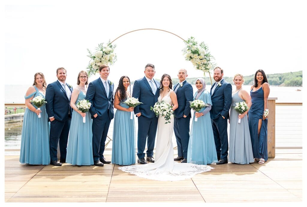 Wedding party gathered together, smiling with ocean views and classic seaside style.