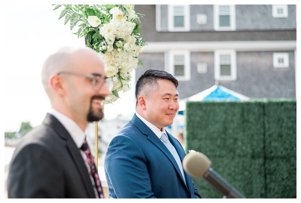 Groom watching the bride approach with an emotional smile during seaside vows.
