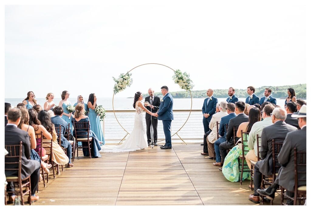 Bride and groom holding hands while exchanging vows in bright natural light.