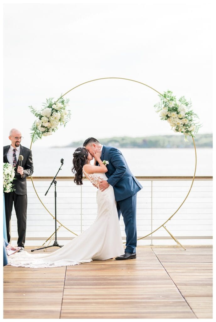 Newlyweds sharing their first kiss with guests applauding in the background.