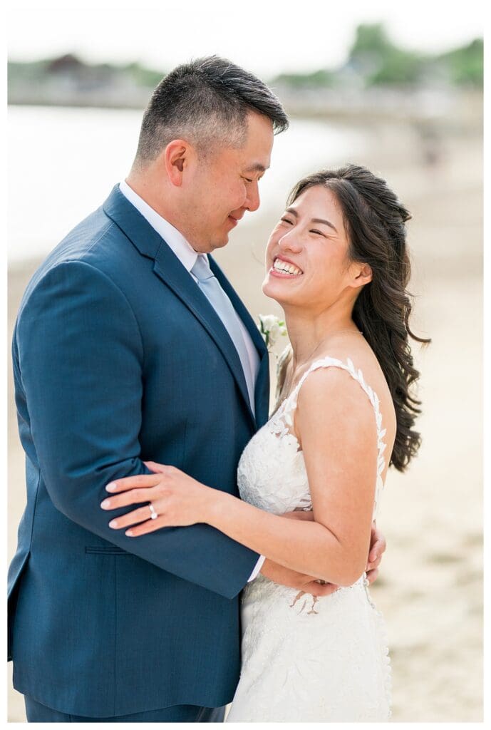 Bride and groom laughing together during wedding portraits outdoors by the ocean.