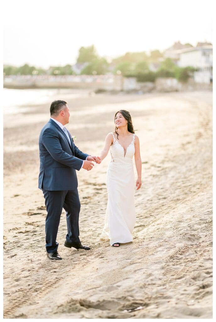 Bride & Groom walking together along the beach, laughing in natural candid photography.