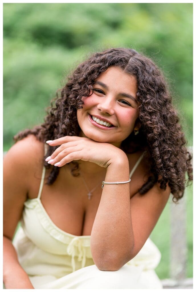 Senior girl in a summery dress with curly hair falling around her face, looking joyful.