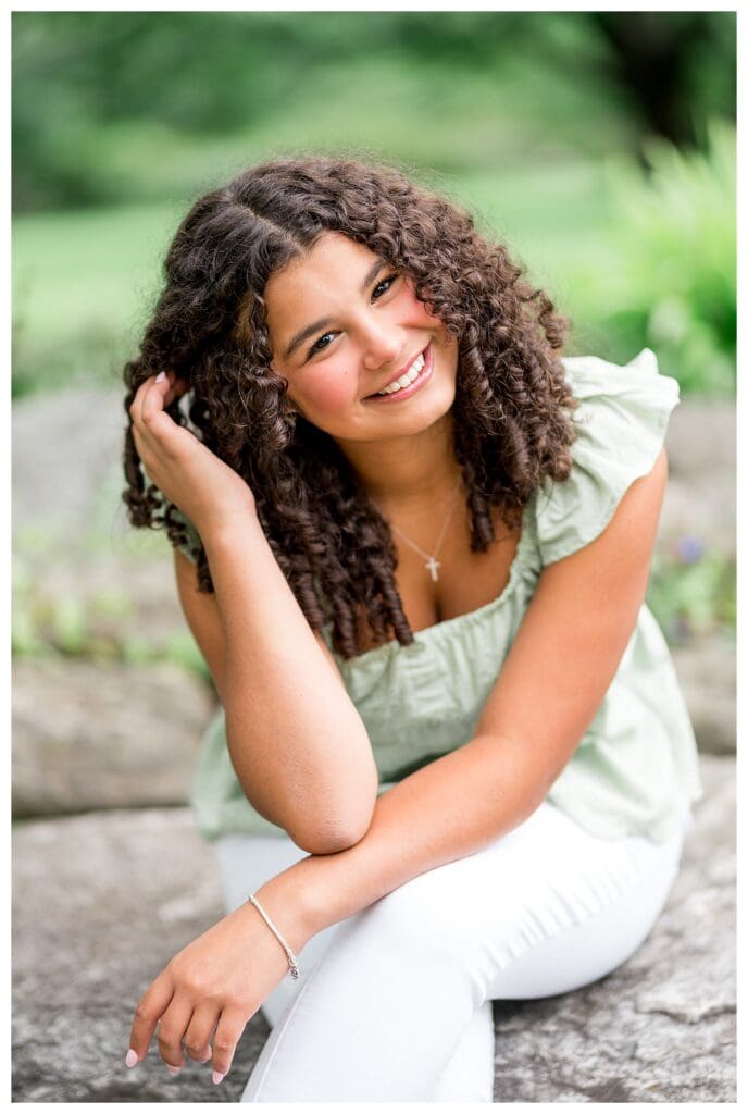 Portrait of Aubrie brushing her curls back, smiling in the summer sunshine.