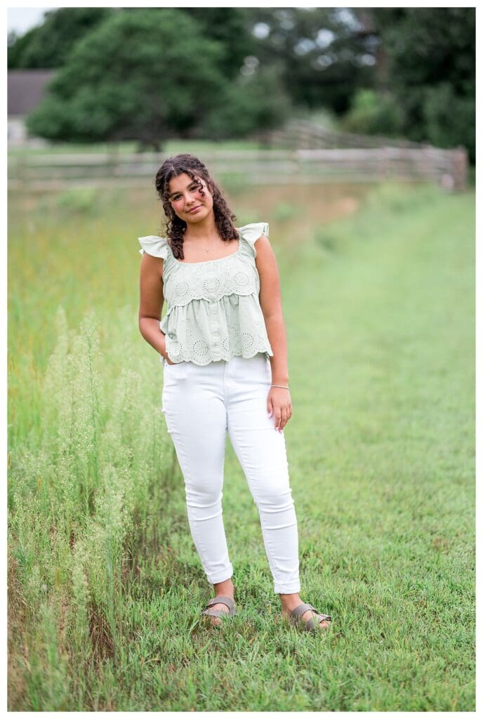 High School Senior standing gracefully in the middle of a wildflower field, soft smile on her face.