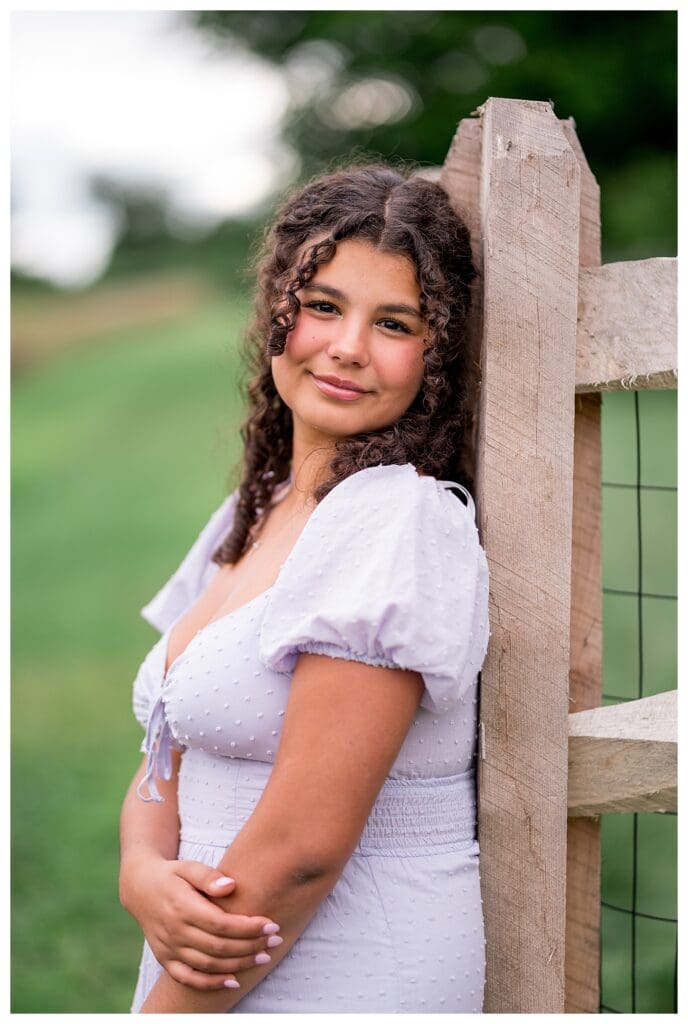 Westford Senior leaning against a wooden fence in a country field, posing with a relaxed smile.