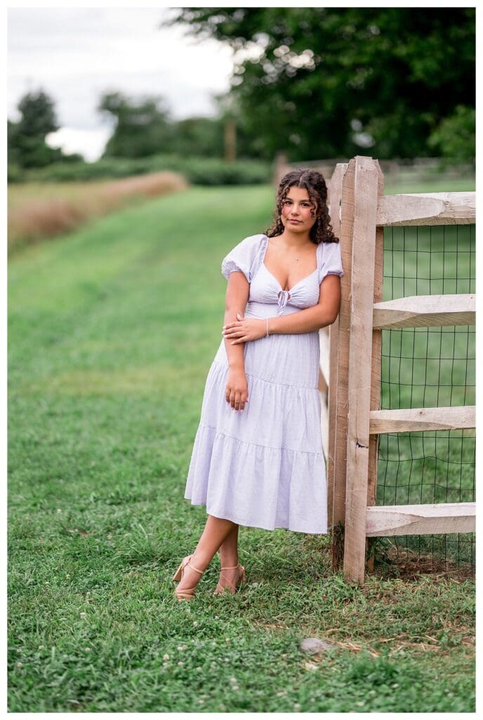 Senior portrait of Aubrie leaning casually against a fence with a natural smile.