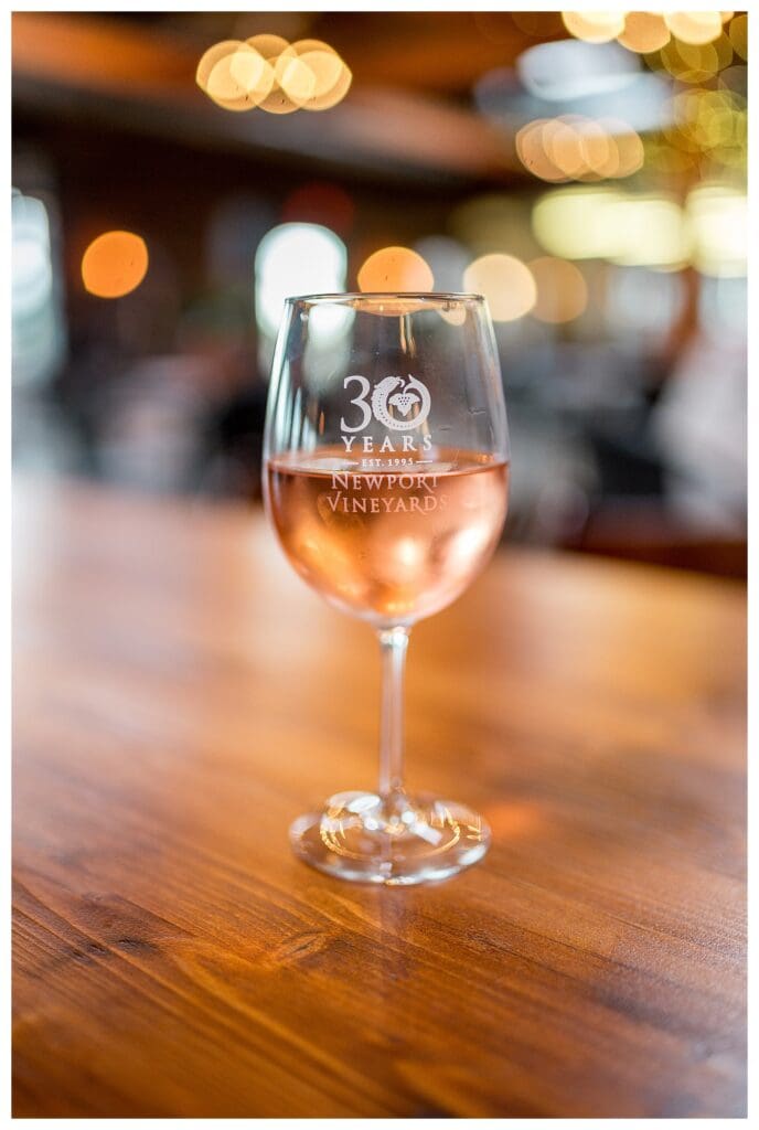 A glass of chilled rosé on a wooden table inside Newport Vineyards with soft lighting in the background.