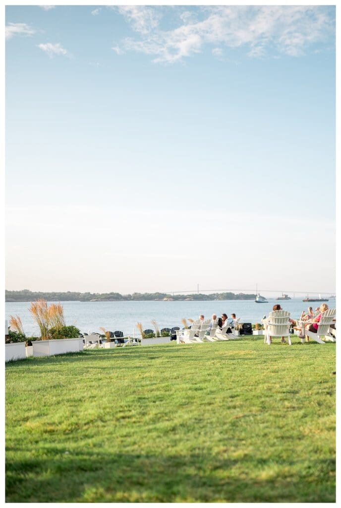 White Adirondack chairs scattered across the lawn at Castle Hill Inn, overlooking the water at sunset.