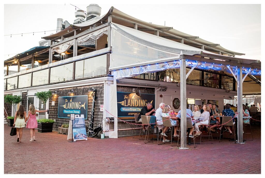 The bustling outdoor patio of The Landing Restaurant in Newport with guests enjoying seafood and drinks near the harbor.