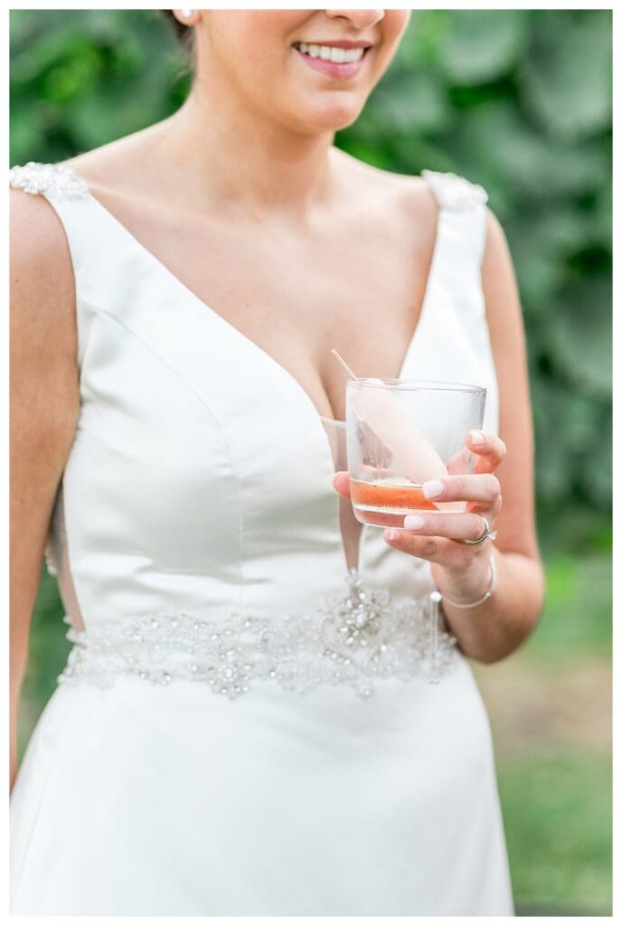 A close-up of a bride holding a glass with a rosé popsicle at Newport Vineyards with grapevines in the background.