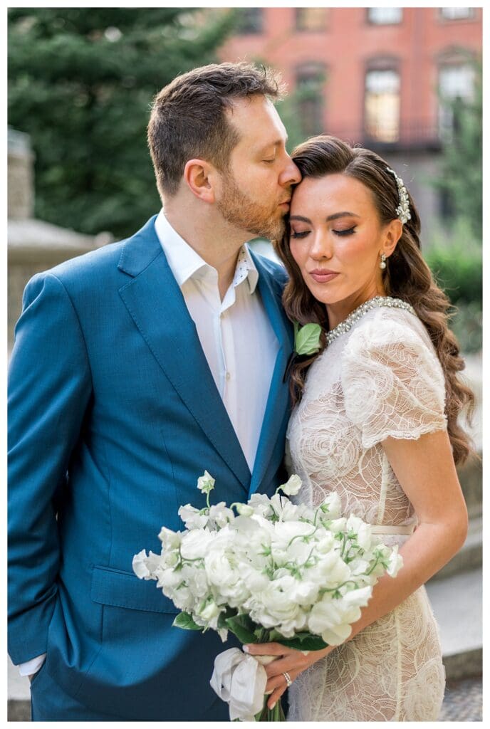 Bride smiling as groom kisses her forehead.