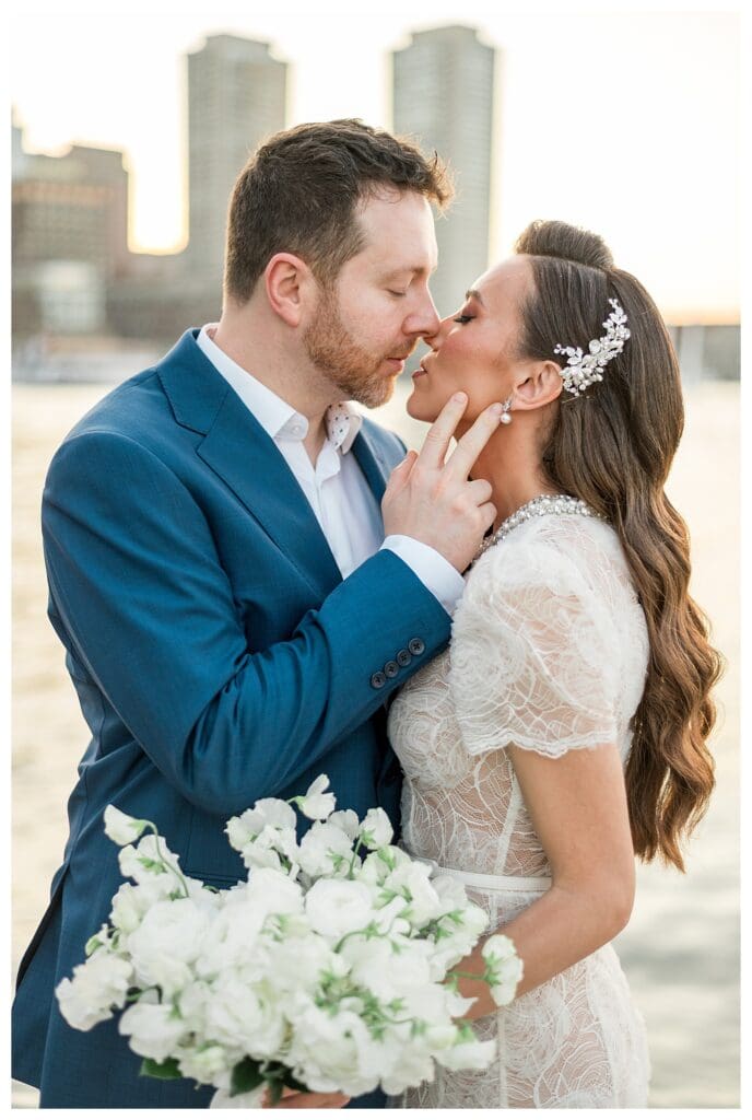 Groom in navy suit kissing bride in lace gown.