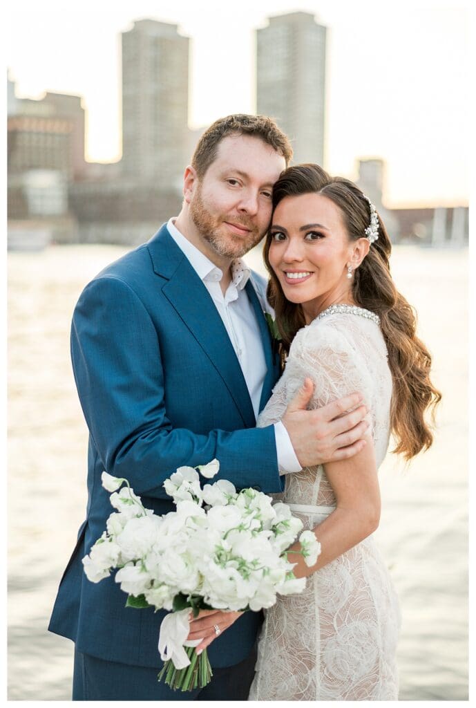 Bride and groom embrace by the Boston Seaport skyline.
