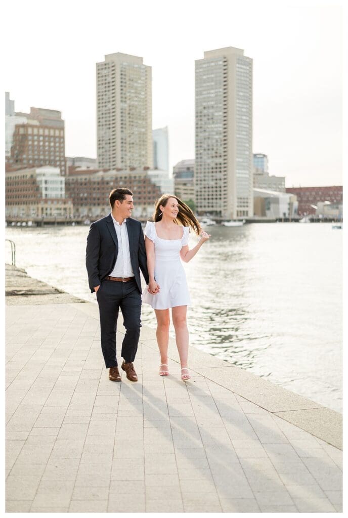 Engaged couple walking hand in hand by the Boston waterfront.