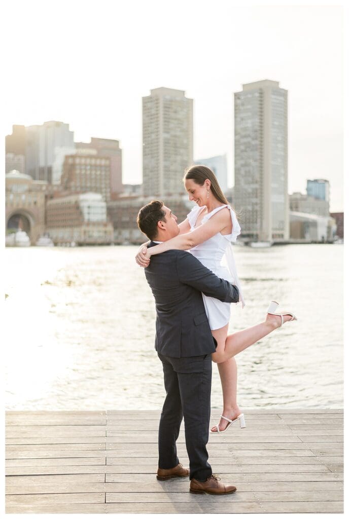 Fiancé lifts his partner as the sun sets over the Boston Seaport.