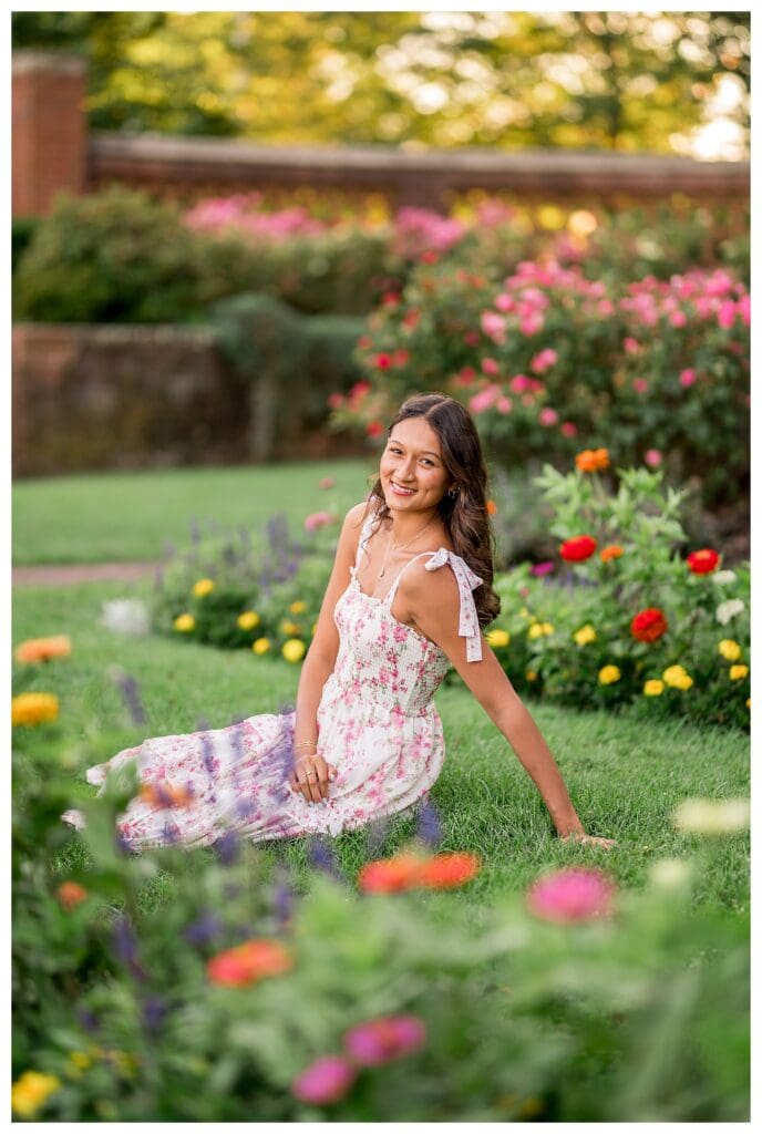 Senior girl sitting among vibrant summer flowers.