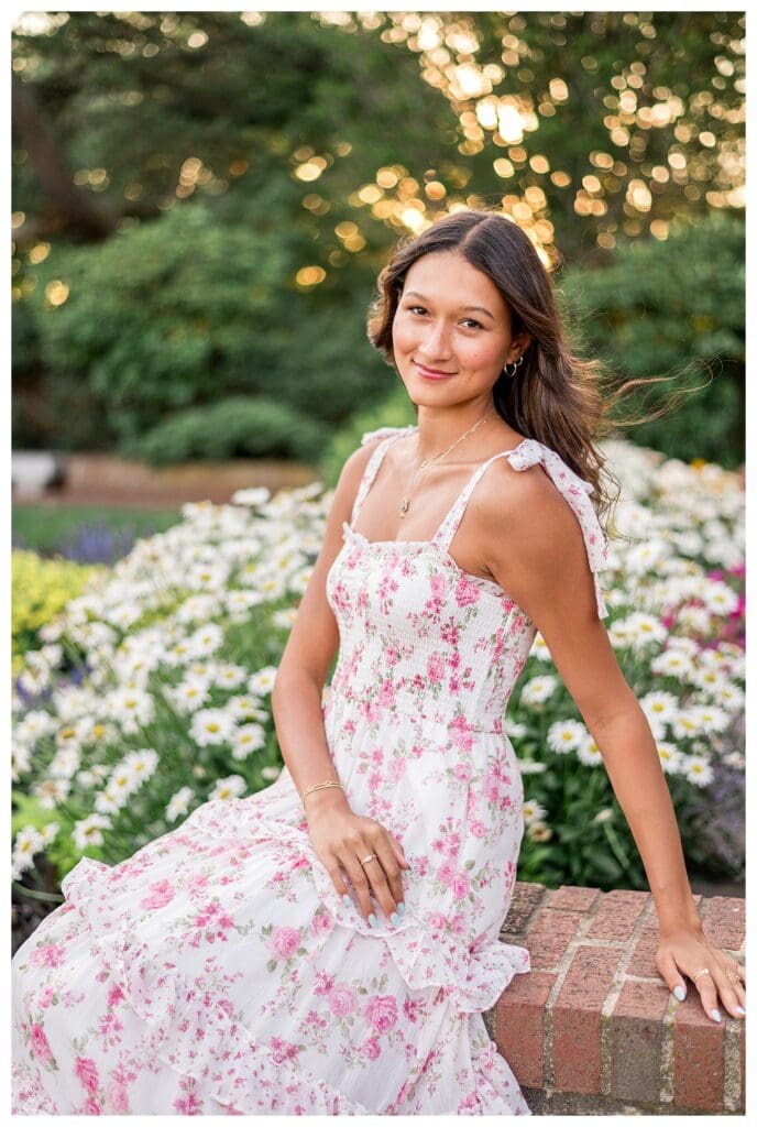 Senior girl posing in a floral sundress with flowers behind her.