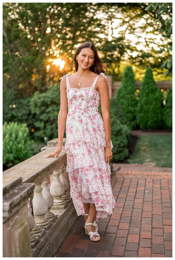 Izzy leaning against a stone wall surrounded by greenery.