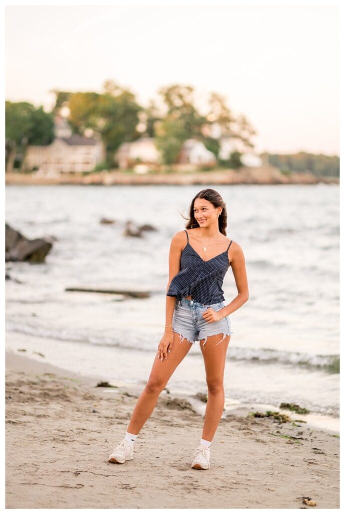 Senior girl standing at the beach shoreline at sunset.