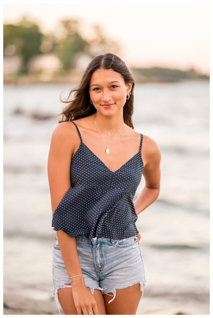 Senior girl smiling with ocean waves behind her.