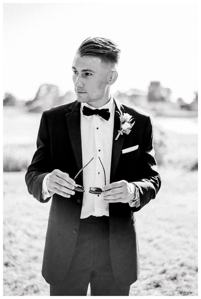 Black and white formal groom portrait in a classic black tuxedo with sunglasses.