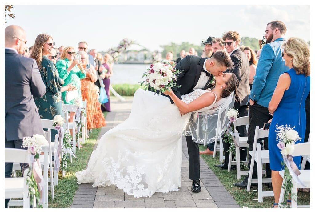Bride and groom sharing a dramatic dip kiss with wedding guests cheering.