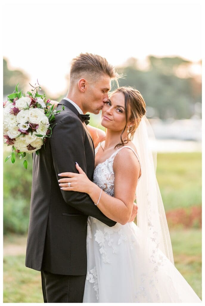 Bride and groom smiling while the bride holds a round floral bouquet.