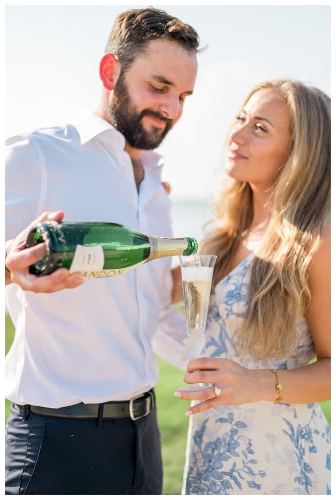 Libby smiling as Reid pours champagne during their Yarmouth proposal celebration