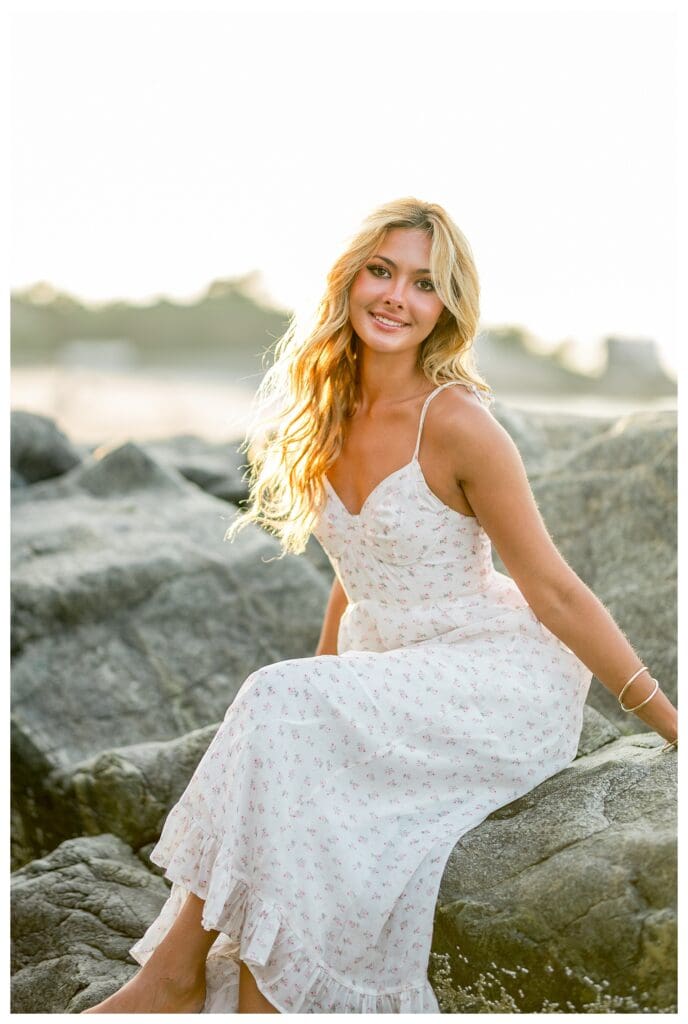 High school senior sitting on coastal rocks during a beach session in Cohasset, MA