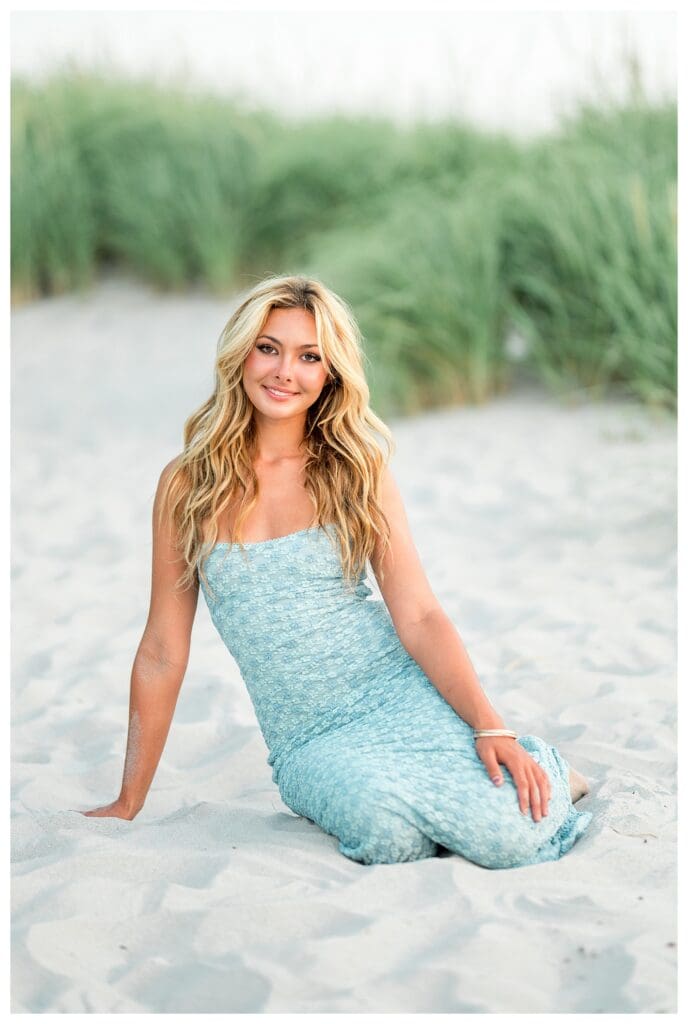 High school senior seated in the sand during a coastal photo session in Cohasset