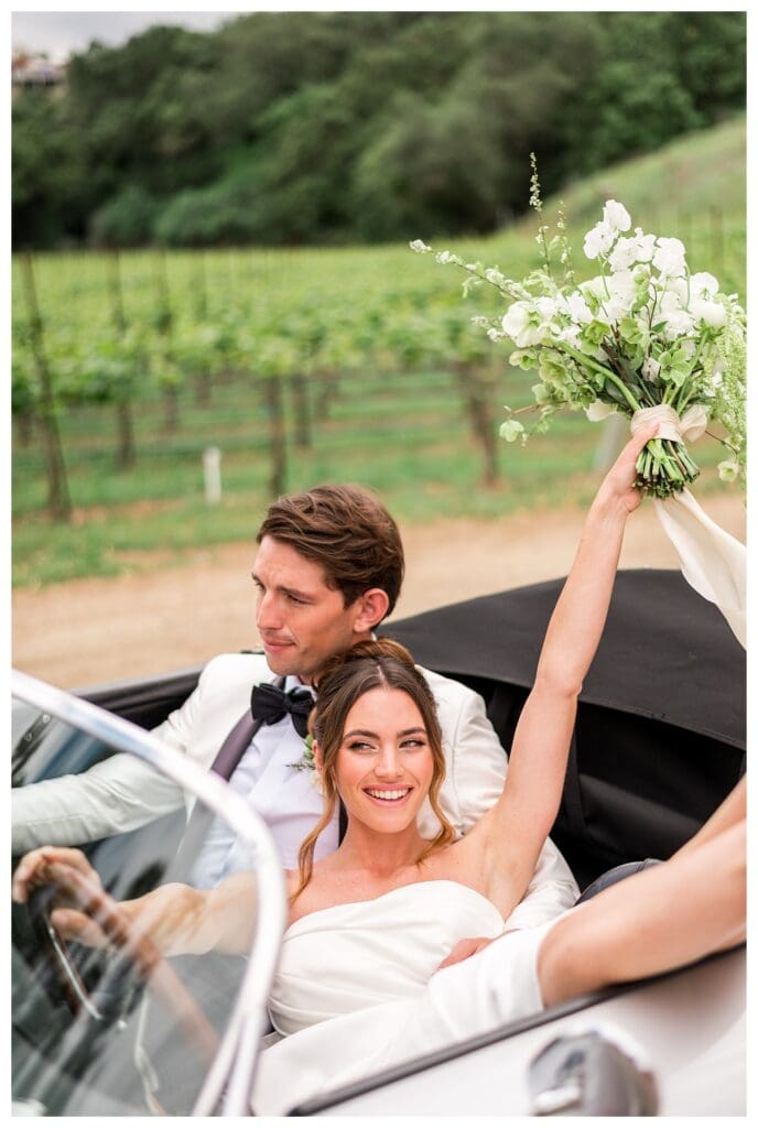 Bride smiling while holding bouquet in a classic convertible at outdoor California destination wedding